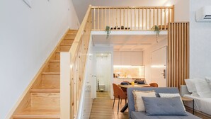 Un intérieur moderne avec un escalier en bois, un coin repas et un espace de vie comprenant un canapé et des coussins.