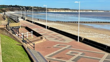 Un paseo marítimo con pavimento estampado, una zona ajardinada y vista al mar.
