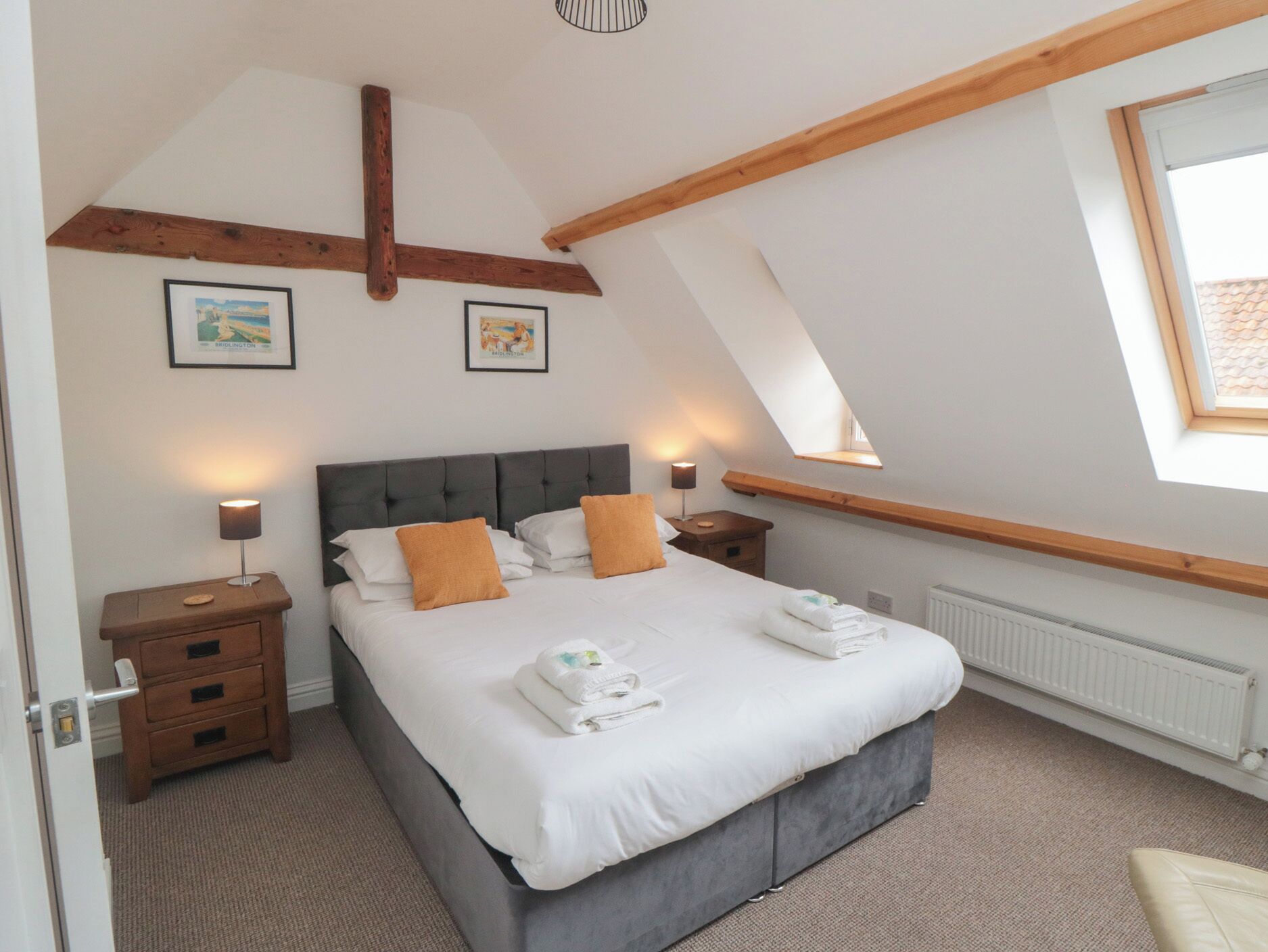 A bedroom with a large bed, two nightstands, a wooden ceiling beam, and a skylight.