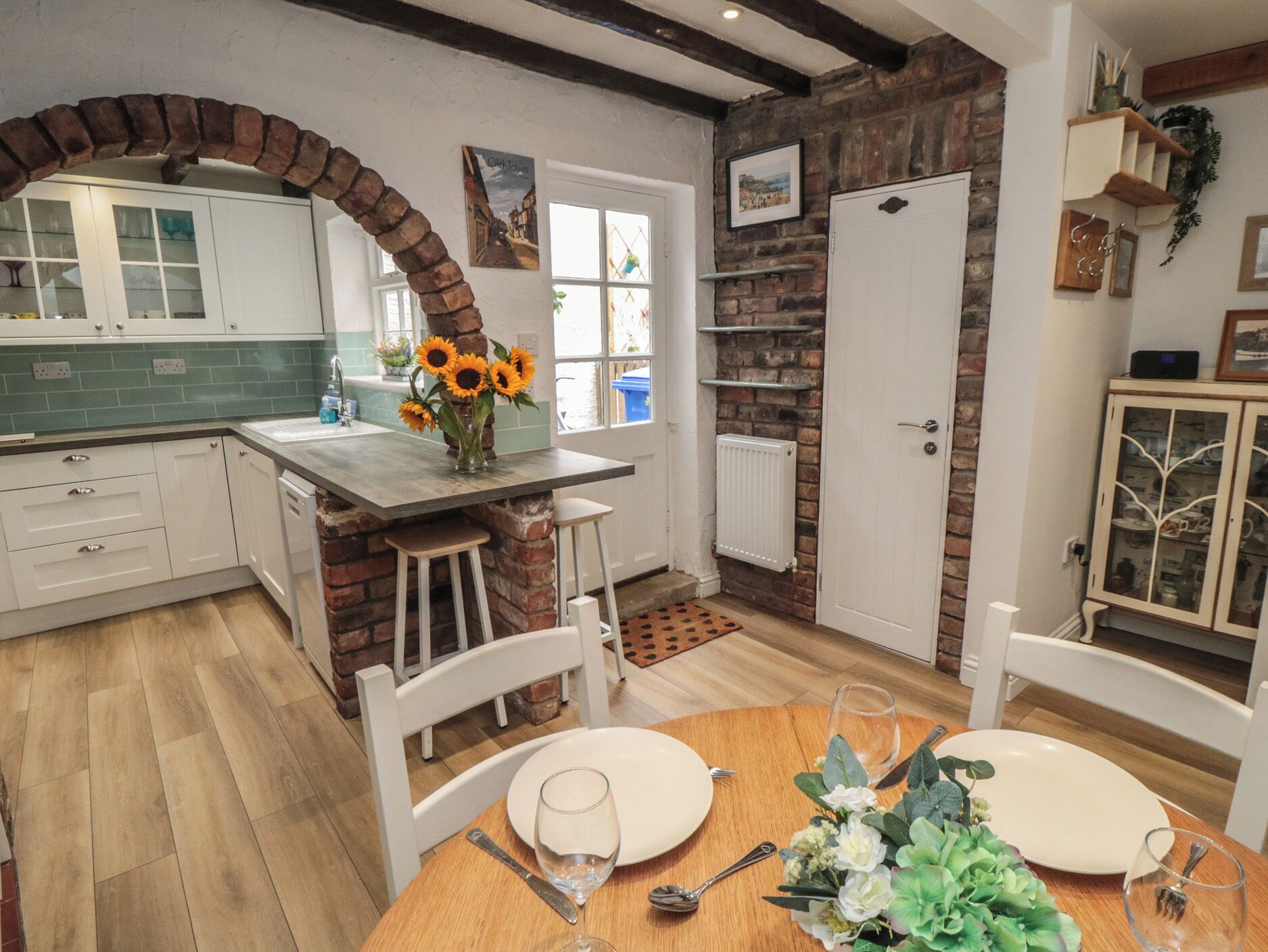 Una cucina con un arco in mattoni, mobili bianchi e un'area pranzo con tavolo apparecchiato per due.