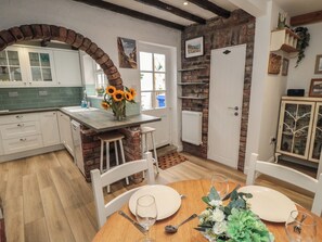 A kitchen with a brick archway, white cabinets, and a dining area with a table set for two. - Bobbies' Retreat, 20 High Street (Bridlington)