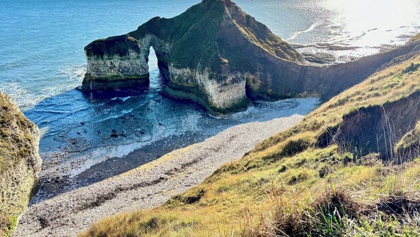Un paysage côtier caractérisé par une formation rocheuse imposante, un sentier étroit et la mer.