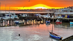 Un port de plaisance avec des bateaux amarrés, une jetée et un coucher de soleil en arrière-plan.