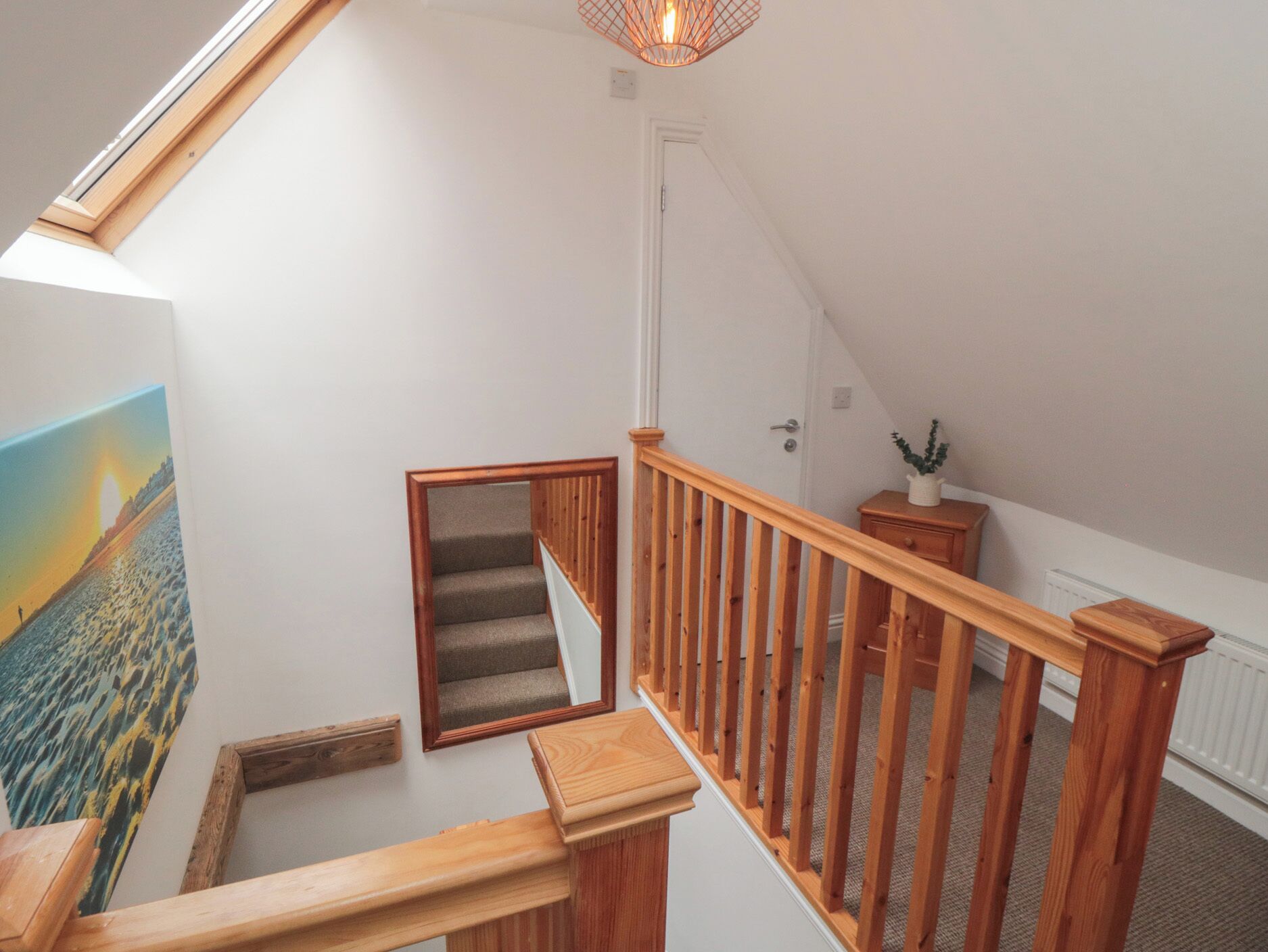 Un escalier en bois avec une rampe, un petit banc en bois, un radiateur et un luminaire fixé au mur.