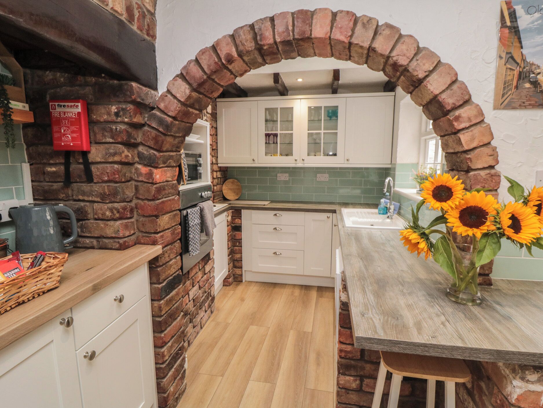 A kitchen with a brick archway, white cabinets, a sink, and a vase with sunflowers.