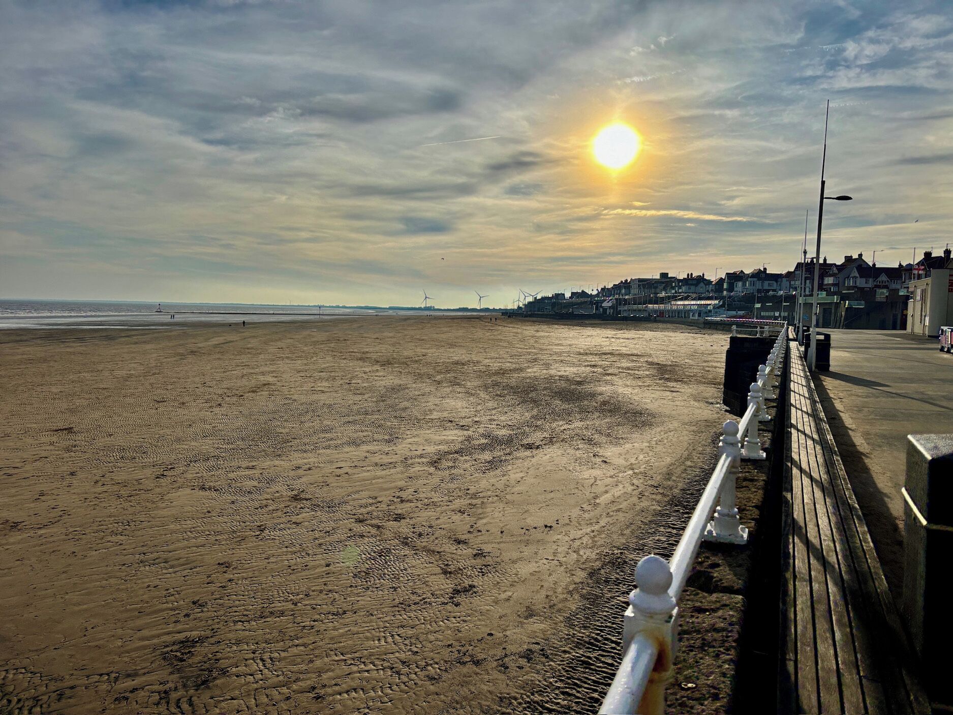 A beach with a wooden walkway, a clear sky, and distant buildings.