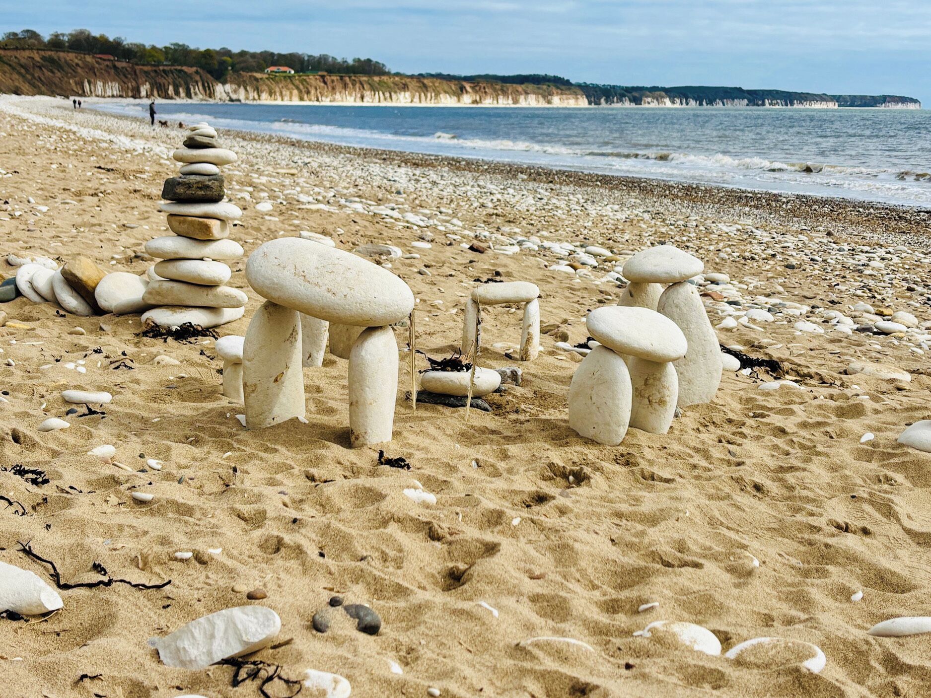 Une plage parsemée d’amas de pierres et de galets, une rive sablonneuse et l’océan en toile de fond.