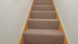 Un escalier dont les marches sont recouvertes de moquette et qui possède des rampes en bois.