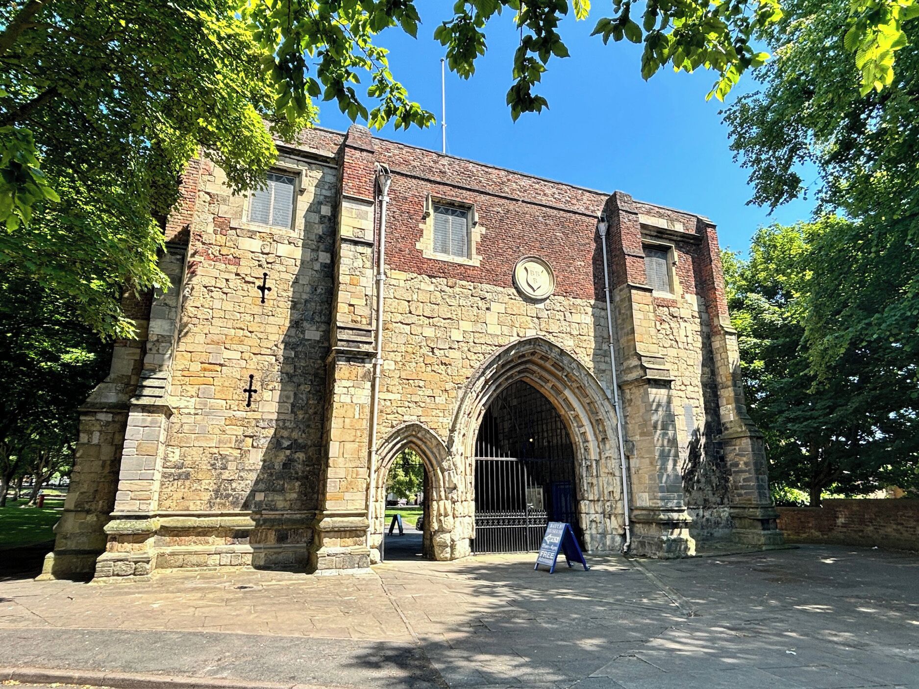 A historic stone building with arched gateways, a clock, and a signboard.