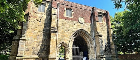 A historic stone building with arched gateways, a clock, and a signboard.