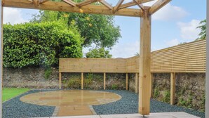 A wooden pergola structure with a circular seating area and a stone wall in the background. - The Oakroyd (Carnforth)