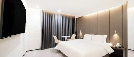 A modern hotel room with a large bed, a flat-screen TV, a small round table, two chairs, and a nightstand with a phone.