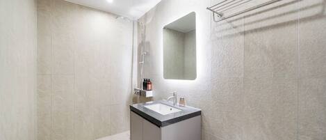 Un baño moderno con ducha, lavamanos con espejo y un perchero para toallas.