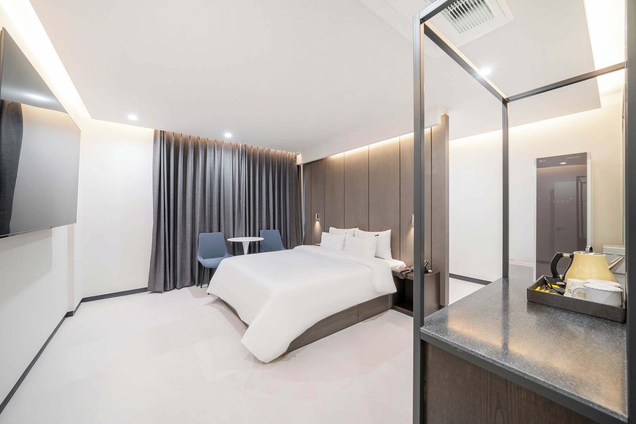 A modern hotel room with a large bed, a desk with a chair, a small table, and a mirror.