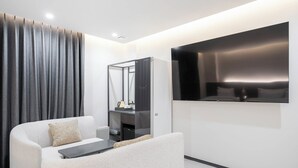 Un salon moderne comprenant un canapé, une table basse, un téléviseur à écran plat fixé au mur et une grande fenêtre avec des rideaux.