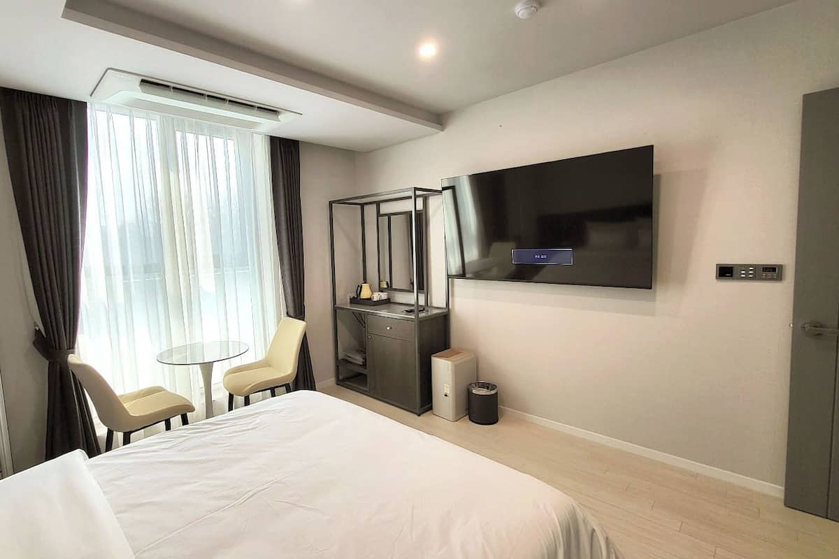 Ein Hotelzimmer mit Bett, Schreibtisch mit Stuhl, einem an der Wand befestigten Fernseher und einem Papierkorb.