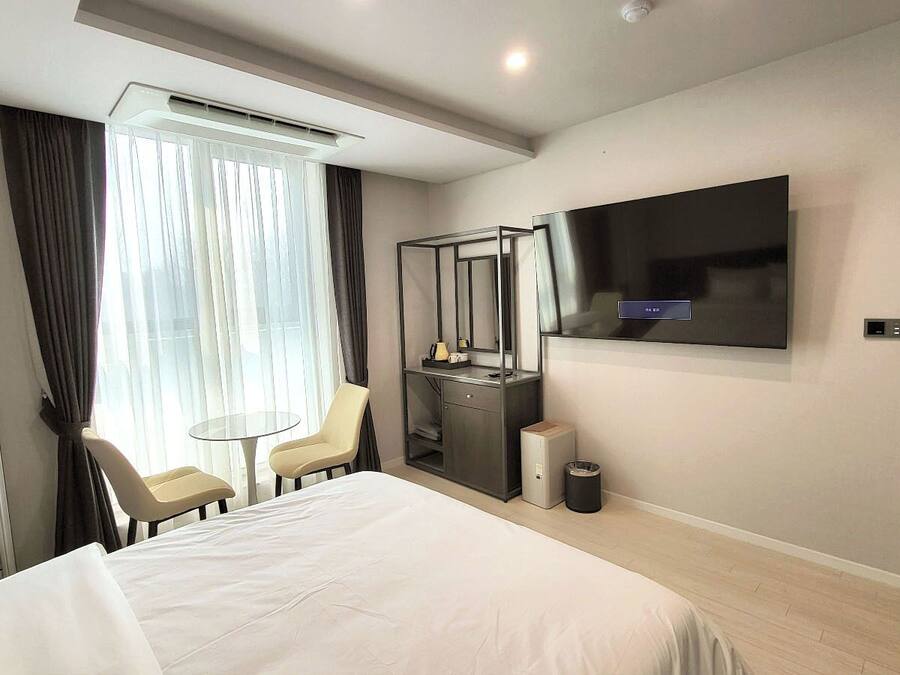 A hotel room with a bed, a desk with a chair, a TV mounted on the wall, and a trash bin.
