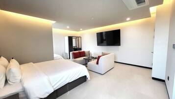 A modern hotel room with a large bed, a sofa, a TV mounted on the wall, and a small table.