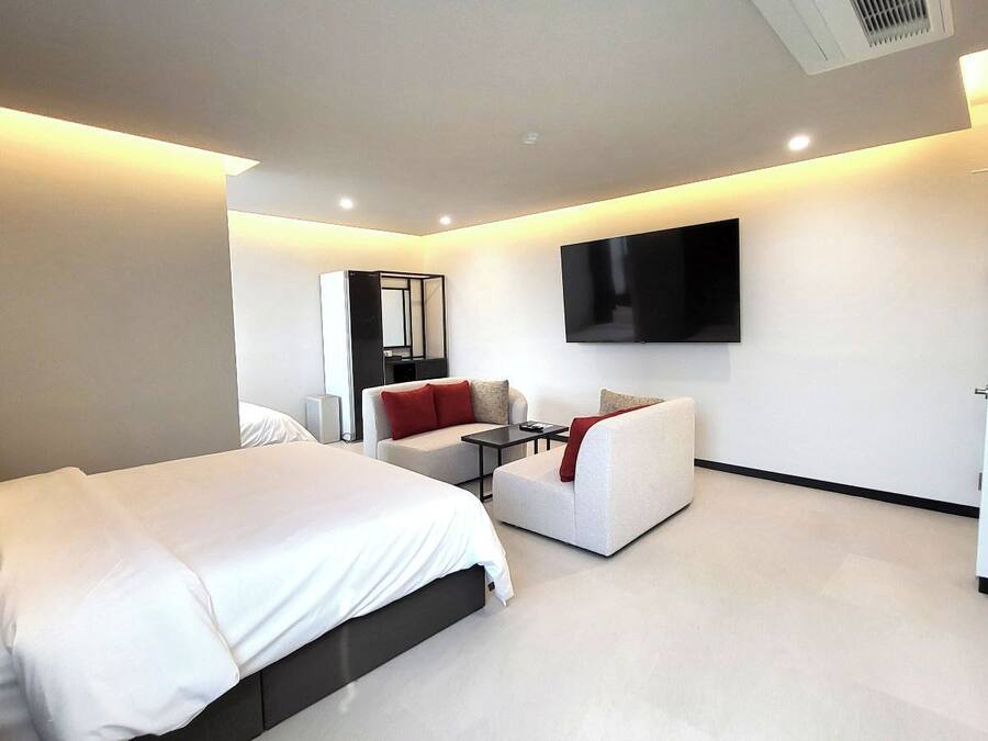 A modern hotel room with a large bed, a sofa, a TV mounted on the wall, and a small table.