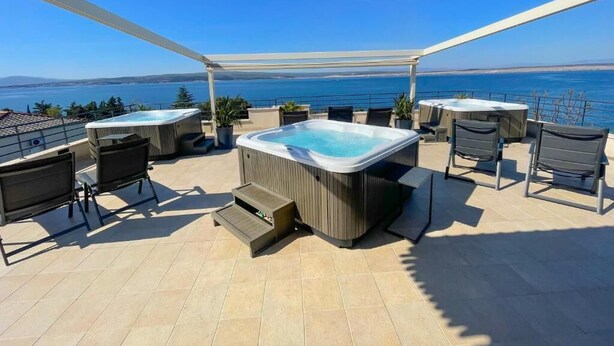 En takterrass med ett bubbelbad, en sittgrupp och utsikt över havet.