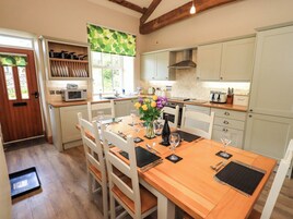 Cocina compacta con armarios de madera, una mesa de comedor lista para cuatro personas y una ventana con vista a zonas verdes.