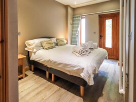 Una cama bien hecha con sábanas blancas y toallas enrolladas, piso de madera y una puerta de madera en una habitación con paredes color beige.