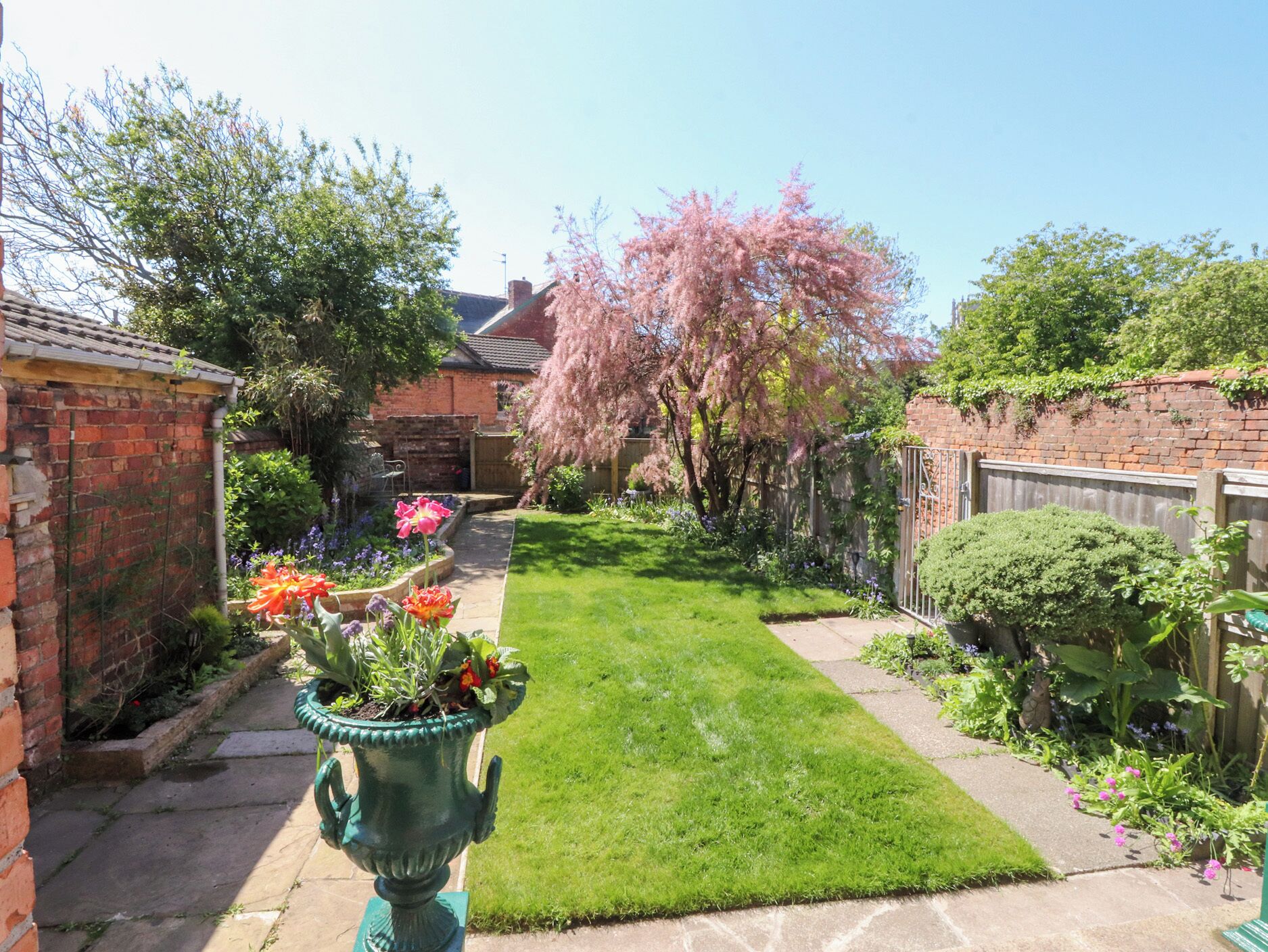 A well-maintained garden with a lawn, flowering plants, and a brick wall.