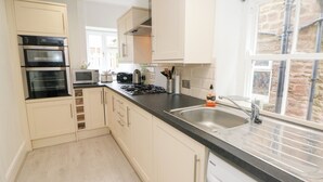 A modern kitchen with white cabinets, a black countertop, a built-in oven, microwave, and dishwasher. - Cherry Tree Cottage (Bakewell)