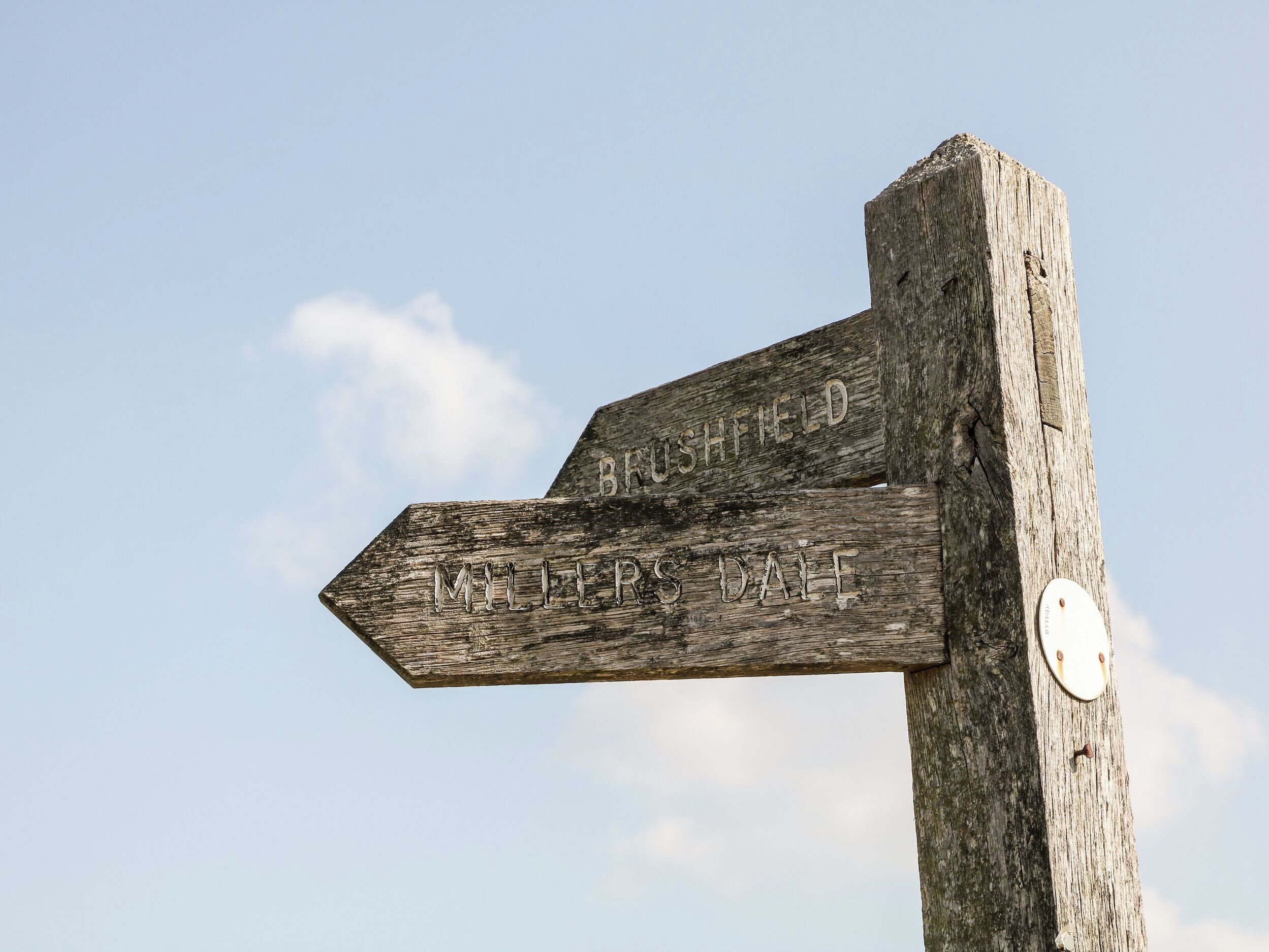 A wooden directional signpost with "BISHOPFIELD" and "MILLERS DALE" engraved on it.