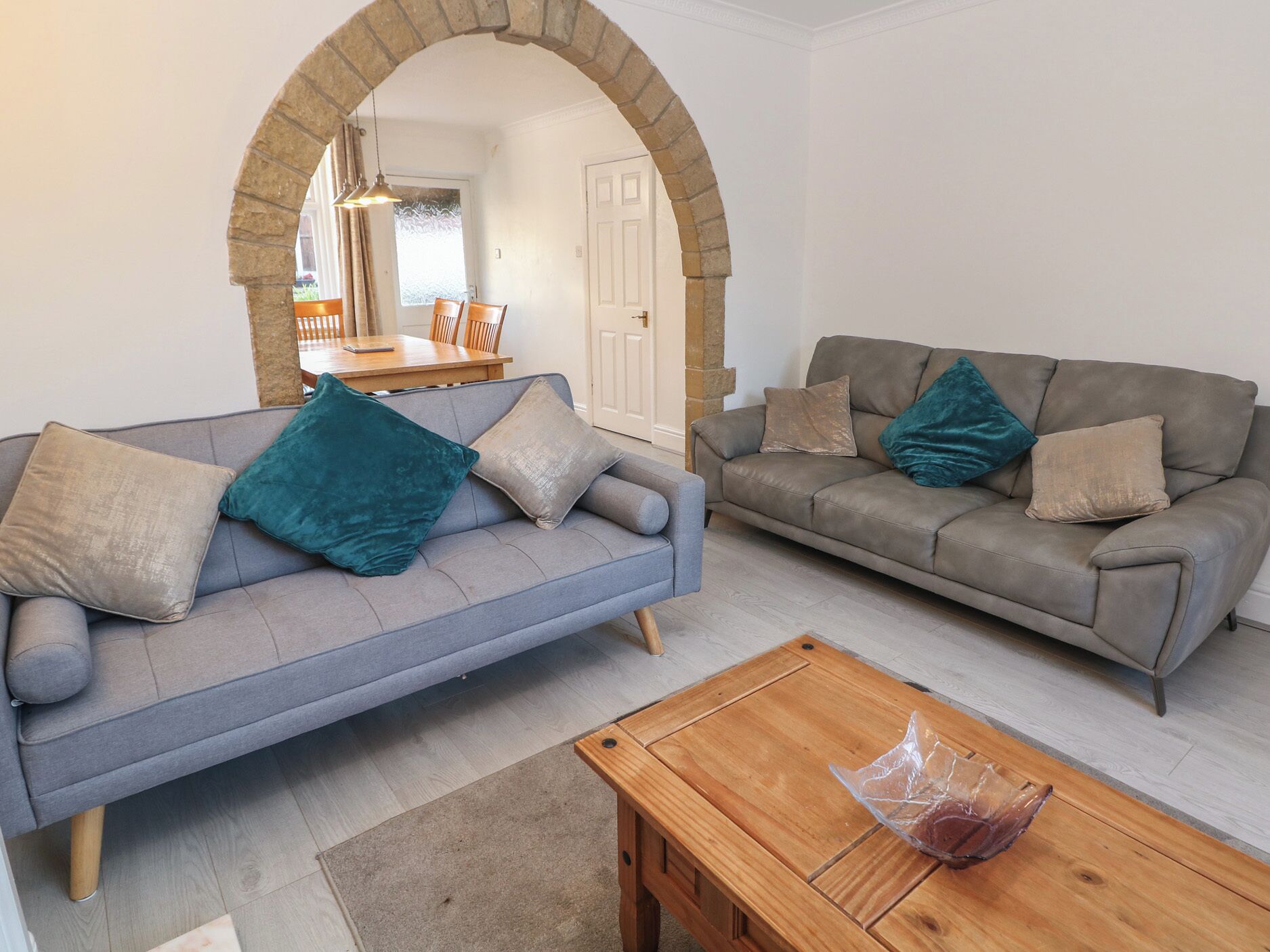 A living room with two sofas, a wooden coffee table, and an arched doorway leading to another room.