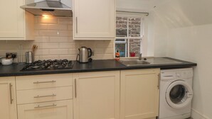 A compact kitchen with a gas stove, kettle, and a built-in washing machine. - Cherry Tree Cottage (Bakewell)