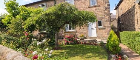 A stone house with a well-maintained garden, a bench, and a small tree.