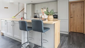 A modern kitchen with a wooden island, two bar stools, and a potted plant. - Gwel Y Fenai (Caernarfon)