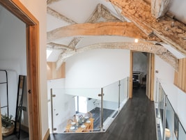 Um interior moderno com vigas de madeira aparentes, uma escada e uma área de jantar com mesa posta para quatro pessoas.
