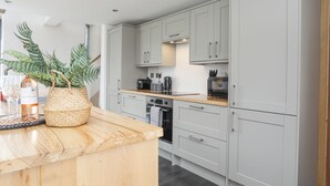 A modern kitchen with light grey cabinets, a wooden countertop, and a built-in oven. - Gwel Y Fenai (Caernarfon)