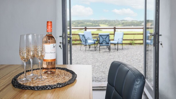 A table with a bottle of Isla Negra wine and glasses, a woven placemat, and a view of an outdoor seating area with chairs and a fence. - Gwel Y Fenai (Caernarfon)