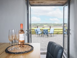 Uma mesa com uma garrafa de vinho Isla Negra e copos, um jogo americano trançado, e vista para uma área de estar externa com cadeiras e cerca.