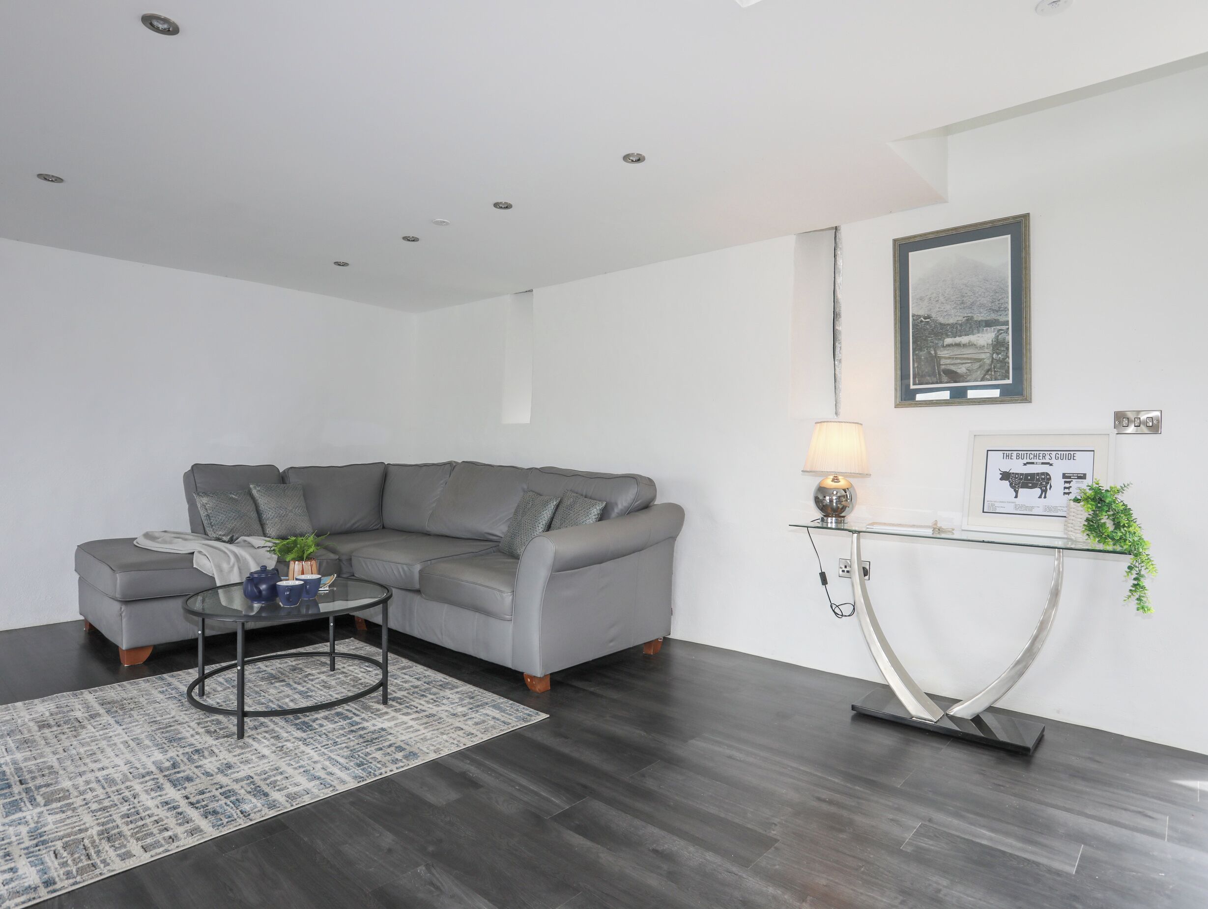 A modern living room with a grey sectional sofa, a glass coffee table, and a small side table with a lamp.
