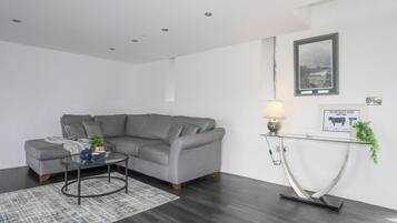 A modern living room with a grey sectional sofa, a glass coffee table, and a small side table with a lamp.
