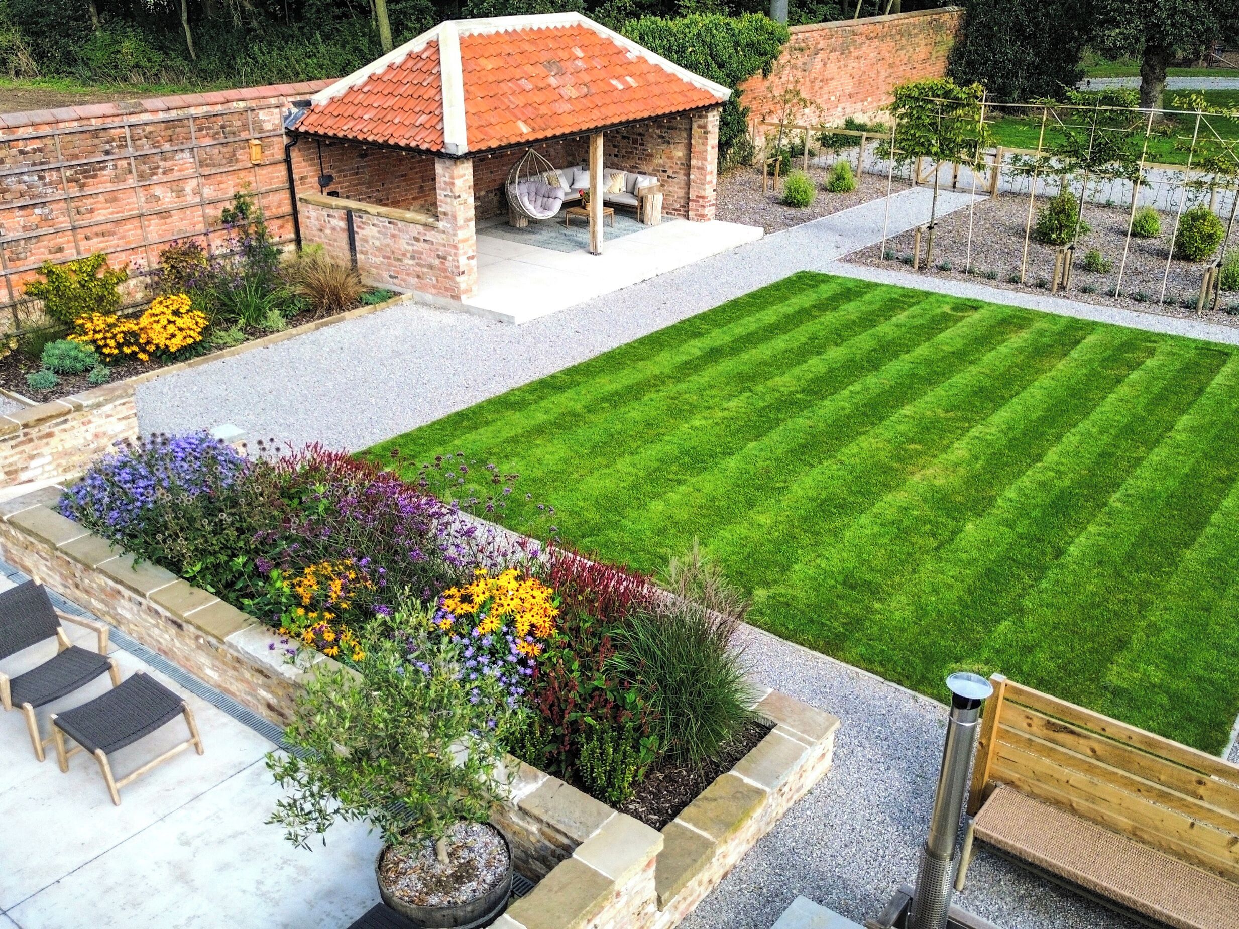 A backyard with a well-maintained lawn, a brick patio area, and a small brick structure with a red roof.