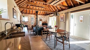 Una cocina rústica con vigas de madera a la vista, un comedor con mesa y sillas de madera, y una zona de estar acogedora con sofá y chimenea.