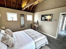 Un dormitorio con cama, tocador con espejo y televisor en la pared.