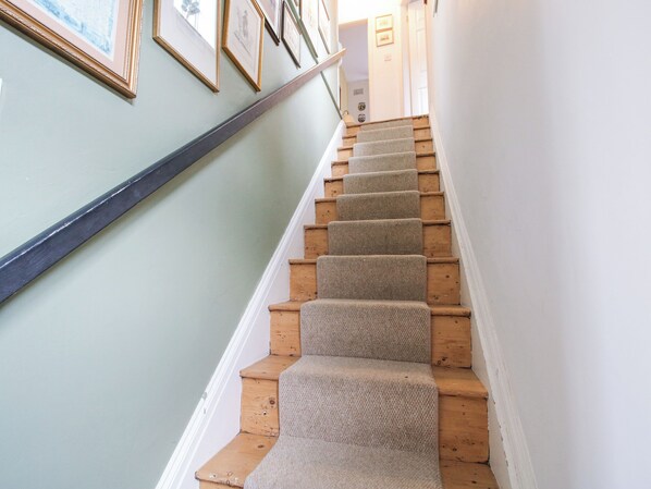 Un escalier avec des marches en bois et des contremarches recouvertes de moquette, menant à un palier où sont accrochées des images encadrées au mur.