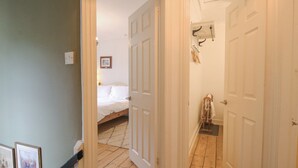 Een gang die leidt naar een slaapkamer met een bed, een deur met een kapstok en een ingelijst schilderij aan de muur.
