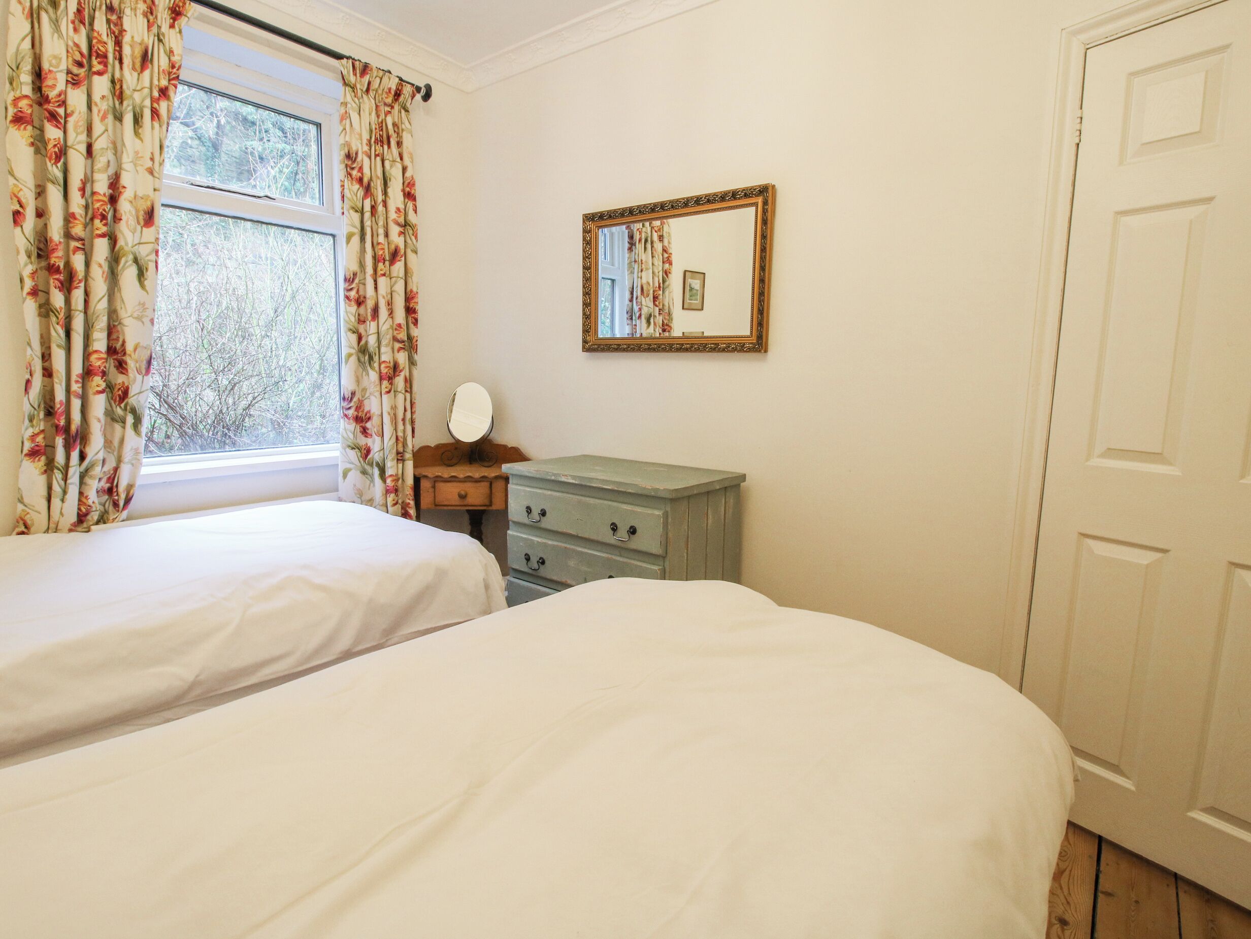 A bedroom with two beds, a dresser, a mirror, and a window with floral curtains.
