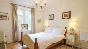 Een slaapkamer met een houten bed, een nachtkastje met een lamp, een raam met gordijnen, en lijstjes met foto's aan de muur.