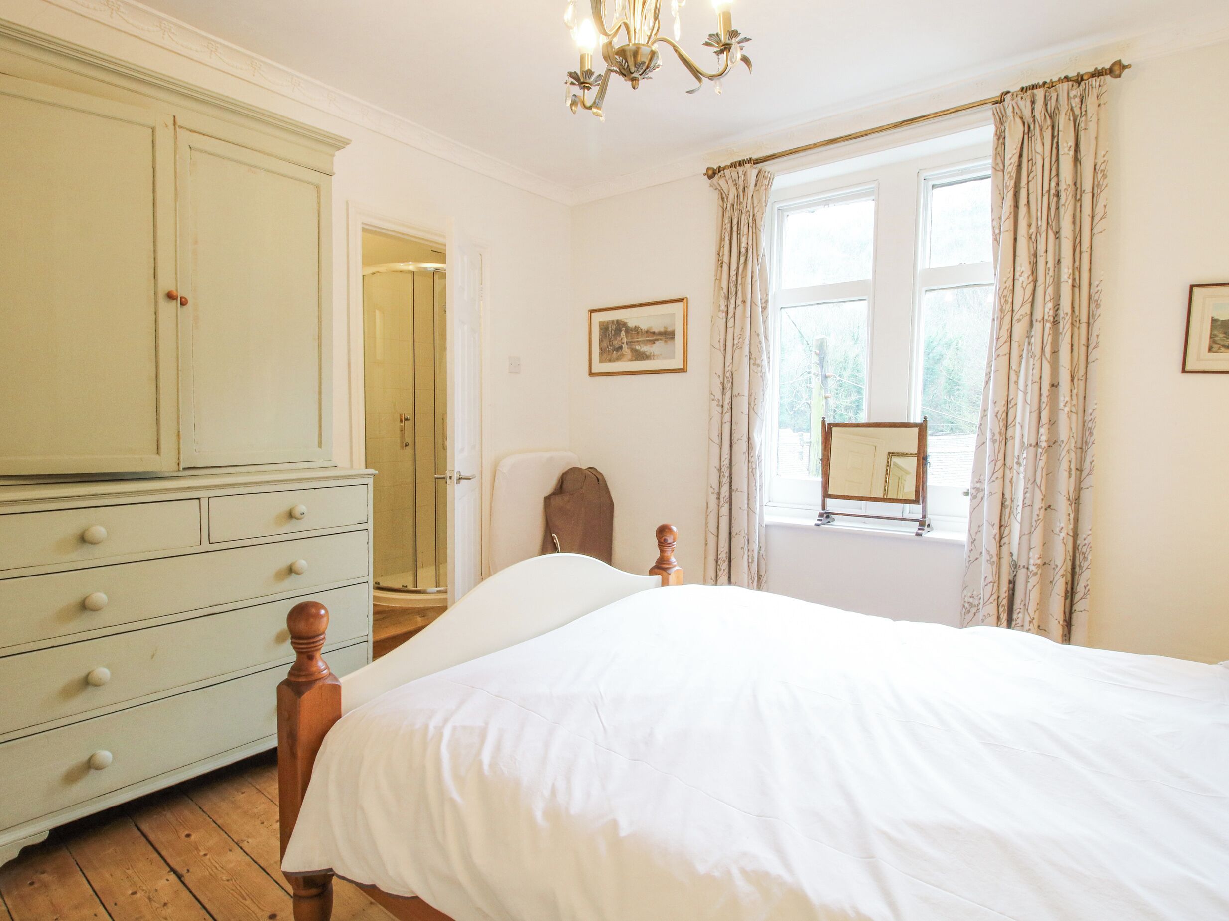 A bedroom with a large bed, a wooden dresser, a window with curtains, and a framed picture on the wall.