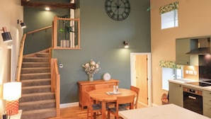 A modern kitchen with a built-in stove, wooden cabinets, and a dining area with a table and chairs. - Old Howgate Barn (Ambleside)
