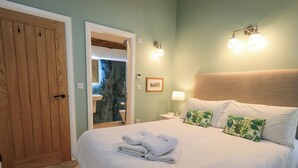A neatly made bed with folded towels, a wooden door, and a bathroom visible through an open door. - Old Howgate Barn (Ambleside)