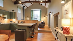 A modern kitchen with wooden beams, a dining area, and a cozy seating space. - Old Howgate Barn (Ambleside)